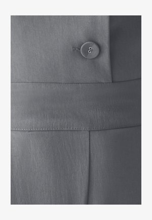 Hall hallide tekstuuriga hall kangas, millel on üks ümmargune nööp ja horisontaalne õmblus, mis näitab kohandatud disaini üksikasju.