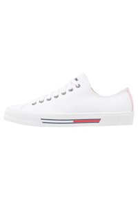 Weißer Sneaker mit niedrigem Schaft, Metallösen, weißen Schnürsenkeln, rotem und blauem Streifen auf der Sohle und rosa Akzent an der Fersenschlaufe.