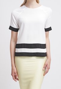 Haut blanc à manches courtes avec des accents noirs sur les manches et des rayures horizontales à l'ourlet, confectionné dans un tissu lisse et léger.