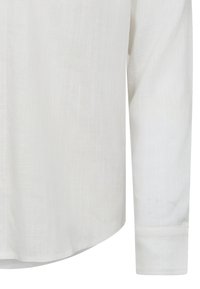 Camicia di lino bianca con maniche lunghe, orlo curvo e texture sottile. Presenta polsini con bottone e un design classico e rilassato.