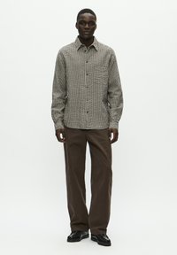 Checkered button-up shirt in black and beige, long sleeves, relaxed fit, paired with brown wide-legged trousers and black shoes.