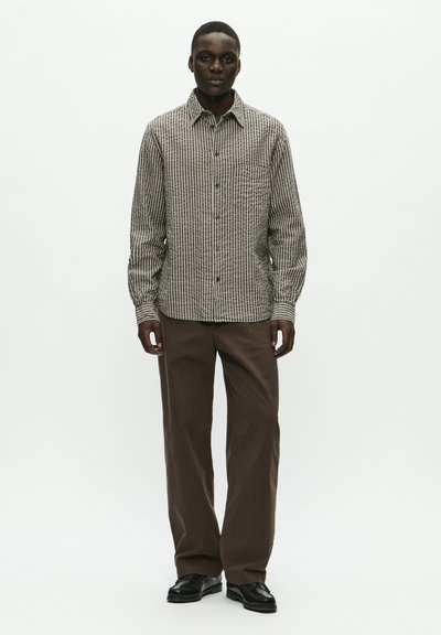 Chemise à carreaux noire et beige, à manches longues, coupe décontractée, associée à un pantalon ample marron et des chaussures noires.