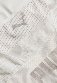 Gros plan sur un tissu blanc texturé avec un logo Puma gris et une partie des grandes lettres du nom de la marque en motif tricoté.
