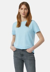 Lichtblauw, kortebloemig katoenen t-shirt met een ronde hals, gecombineerd met donkergrijze jeans. De stof lijkt zacht met een gladde textuur.