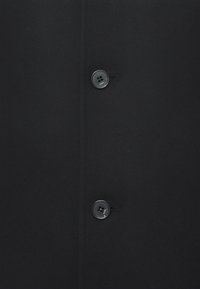 Material negru cu două butoane negre cusute vertical, fiecare buton gravat cu cuvântul "KARL."