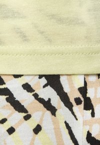 Lichtgele stof aan de bovenkant, daaronder bevindt zich een gemusterde stof met zwarte, beige en witte vormen. Geverfde brei met zichtbare stiksels.