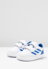 Vita sneakers med blå detaljer, utrustade med två kardborreband, en strukturerad textilovandel och tre blå ränder på sidan. Gummisula.