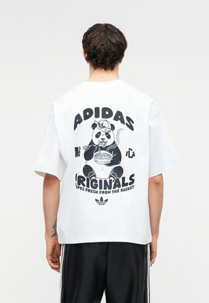 Persoană purtând un tricou alb Adidas cu un desen negru cu un panda care mănâncă tăiței și textul „Adidas Originals” pe spate.