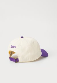 Baseballová čiapka s krémovým bavlneným telom a fialovým okrajom. Obsahuje fialové prešívanie a nastaviteľný pásik na zadnej strane.