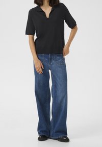 Polo noir à manches courtes avec col en V, associé à un jean en denim bleu taille haute à jambes larges. Texture lisse avec surpiqûres contrastantes.