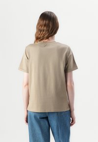 Lys brun, kortermet T-skjorte med rund hals. Myk tekstur og rett snitt, kombinert med blå denimjeans for et avslappet utseende.