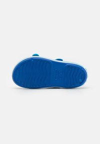 Scarpa di gomma blu con suola texturizzata caratterizzata da motivi a onda e dettagli in rilievo, completata da un bordo bianco attorno al perimetro.