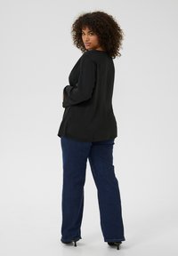 Sort, let bluse med afslappet pasform og lange, flagrende ærmer, parret med mørkeblå flagrende jeans og høje hæle.