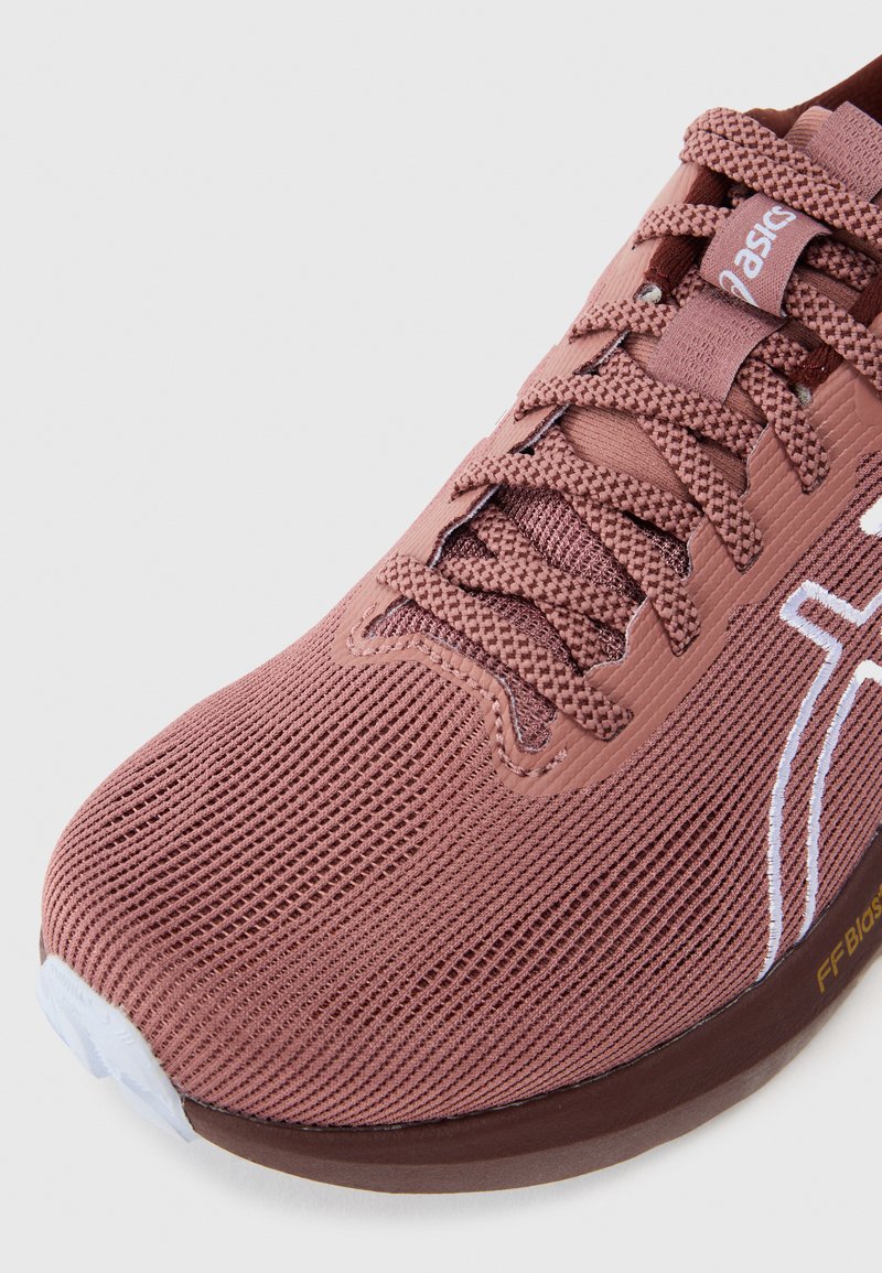 Hellrosa Sportschuh mit einem atmungsaktiven Obermaterial aus Mesh, strukturierten Schnürsenkeln und einer gepolsterten Sohle. Ausgestattet mit einem weißen Logo und dezenten Details.