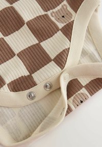 Close-up of ribbed fabric baby clothing with brown and cream check pattern and smiling bear faces, featuring snap button fasteners.
