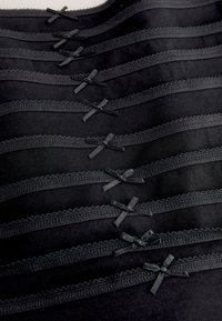 Intimo nero con delicati bordi in pizzo e fiocchi di raso, disposti in file orizzontali sovrapposte, che mostrano un tessuto liscio e una consistenza uniforme.