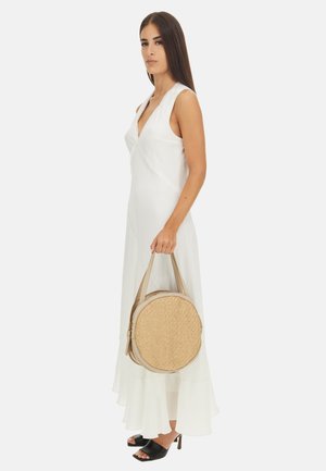 Borsa rotonda in paglia intrecciata con una cerniera e manici beige. La borsa presenta un materiale naturale dal texture che completa un vestito bianco fluente.