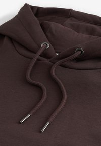 Sudadera con capucha marrón de tejido grueso, con cordones flexibles y ojales metálicos en el cuello.
