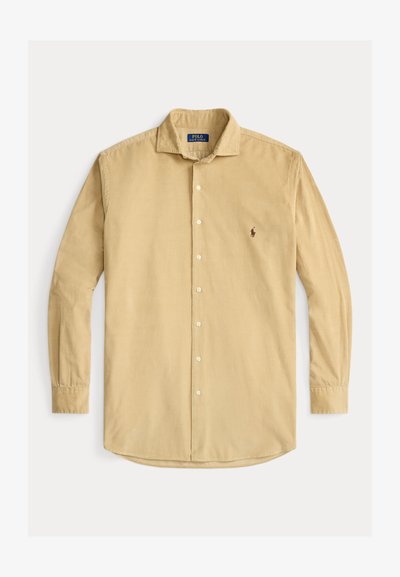 Camisa de veludo côr creme de mangas compridas, com fecho de botões à frente, colarinho e pequeno logótipo bordado no lado esquerdo do peito.