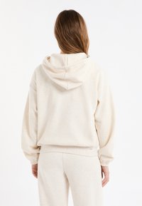 Sweat à capuche de couleur crème en tissu doux et texturé, à la coupe ample, avec une capuche surdimensionnée et des poignets élastiques, assorti à un pantalon coordonné.