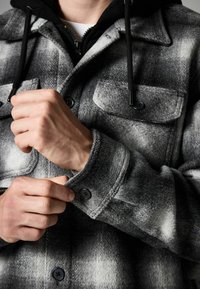 Grijze en zwarte flanellen shirtjacket met knoopzakken, textuurstof en een dikke kraag; heeft verstelbare manchetten en een gevoerde capuchonlaag.