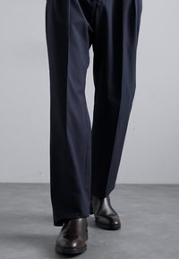 Pantalones navy de corte holgado, con una textura suave; combinados con botas de cuero marrón oscuro. Diseño minimalista, sin patrones visibles.
