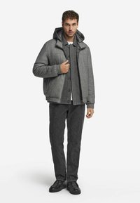 Graue gepolsterte Jacke mit Kapuze, Frontreißverschluss und Rippbündchen, über einem grauen Pullover und dunkelgrauen Hosen geschichtet, kombiniert mit schwarzen Schuhen.