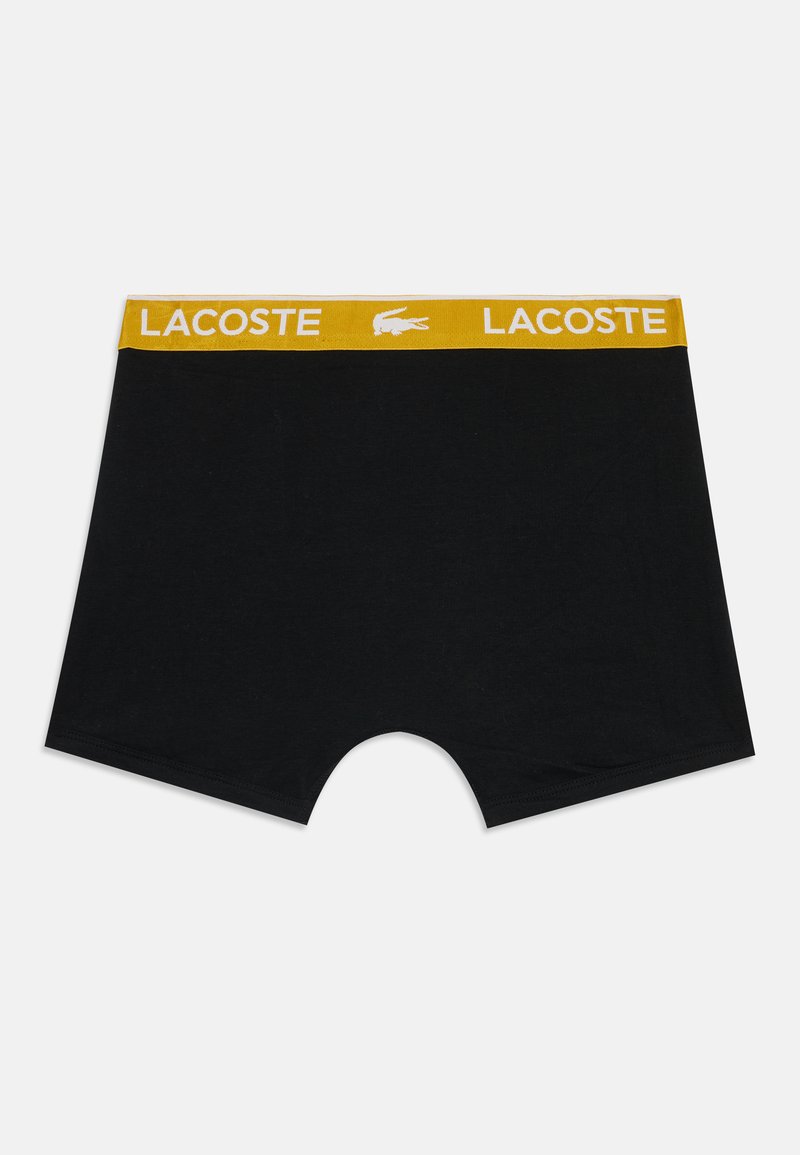 Boxers noirs pour hommes avec ceinture élastique jaune comportant le texte blanc Lacoste et le logo crocodile centré.