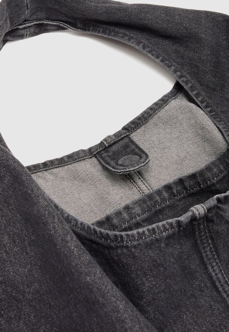 Nahaufnahme des Kragens einer schwarzen Denimjacke mit sichtbaren Steppnähten und Stoffschlaufe am inneren Halsausschnitt.