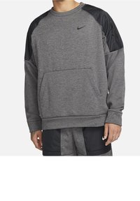 Homme portant un sweat-shirt Nike gris et noir assorti à un short, les mains détendues le long du corps, sur un fond blanc uni.