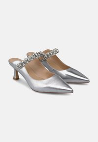 Tacones slingback plateados de punta afilada con un pequeño tacón bloque y una correa adornada a lo largo del empeine. Textura metálica suave, diseño elegante.