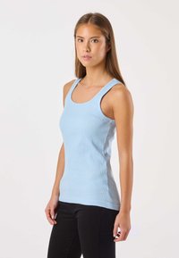 Vaaleansininen ribbineuloksinen toppi, leveillä olkaimilla, pyöreällä pääntielle ja istuvalla mallilla. Yhdistetty mustiin housuihin ja minimalistisiin yksityiskohtiin.