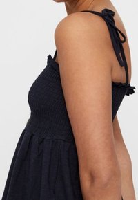 Navyblaues Sommerkleid mit gerafftem Oberteil, dünnen Schulterträgern und fließendem Rock. Weicher Stoff mit einem einfachen, lässigen Design.