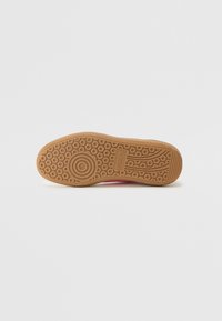 Semelle de sneaker en caoutchouc de couleur gomme avec des motifs de bande de roulement circulaires et linéaires. Présente un accent rose sur le côté. Texturée pour une bonne adhérence.