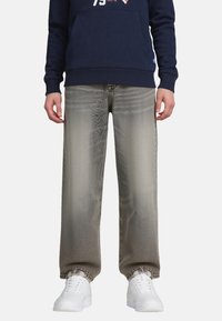 Persoon in grijs vervaagde rechte spijkerbroek, witte sneakers en een marineblauwe sweatshirt met een voorzak.