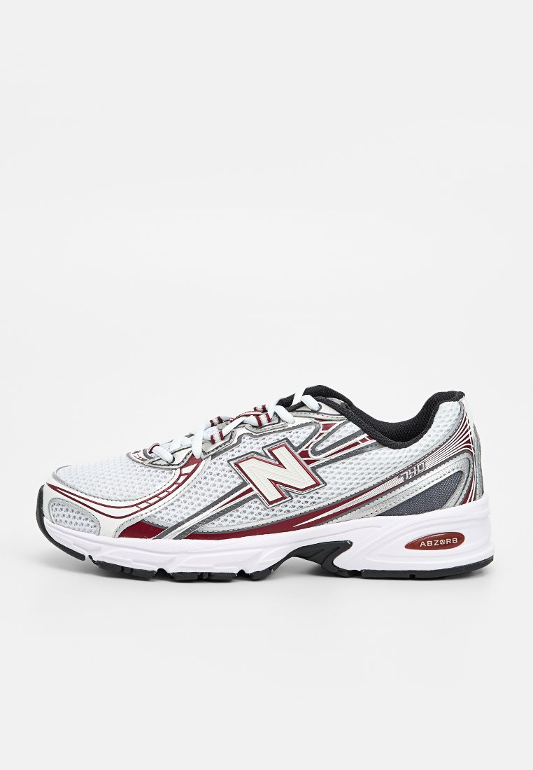 Chaussure de sport en mesh blanc avec des accents rouges et noirs. Présente une surface texturée, une semelle épaisse et un logo "N" bien en vue.
