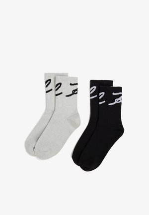 Deux paires de chaussettes côtelées : une grise avec un texte noir et une noire avec un texte gris. Les deux ont une hauteur de cheville et une texture lisse.