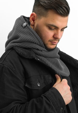 Gray knitted scarf wrapped around the neck, featuring a textured pattern. Worn with a black jacket, showcasing a soft-lined collar.