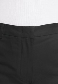 Czarne spodnie wykonane z gładkiej tkaniny, z płaskim przodem, szerokim pasem i subtelnymi przeszyciami. Brak widocznych kieszeni.