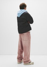 Sort dunjakke med en lyseblå hætte, kombineret med lyserøde, løstsiddende jeans og beige sneakers i flere nuancer.