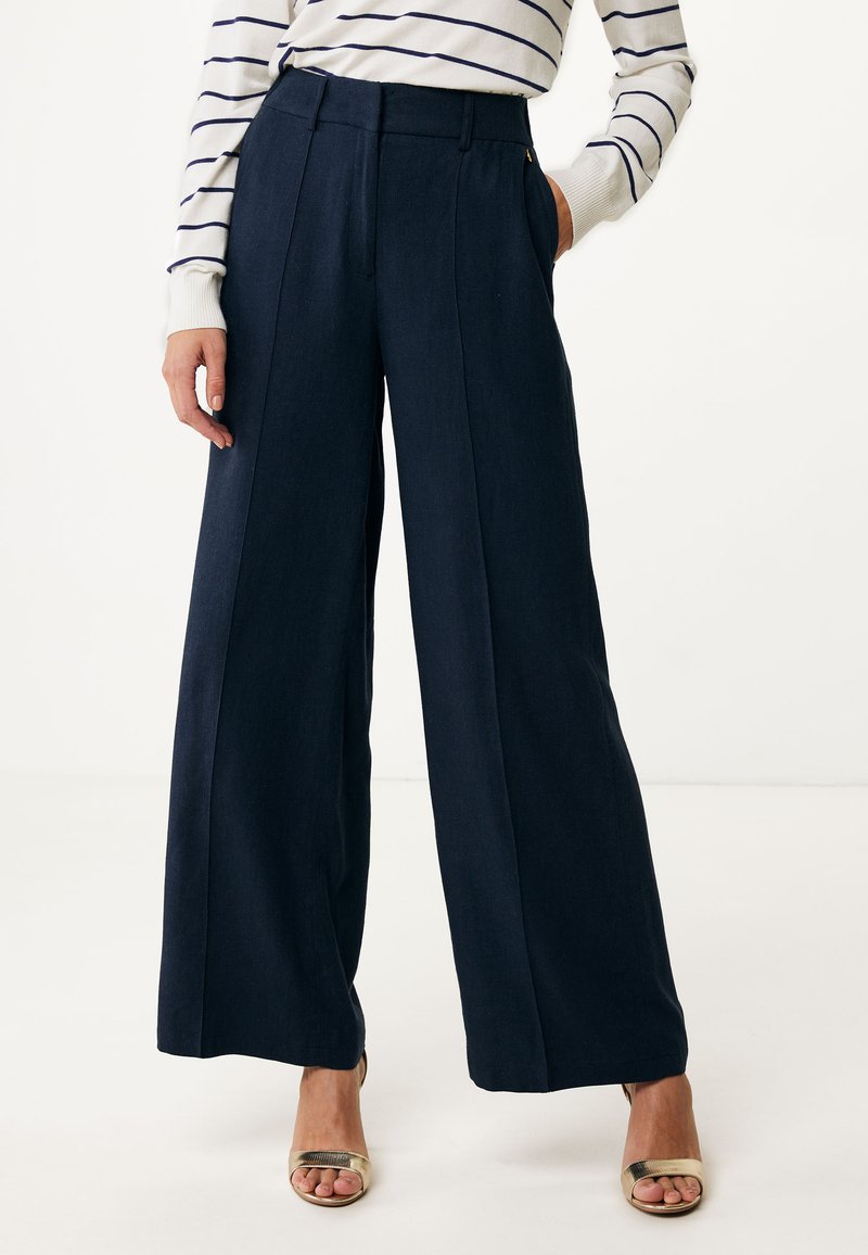 Marineblauwe wijde broek gemaakt van een licht-textuurlijke stof, met een hoge taille, voorplooien en zijzakken, gecombineerd met sandalen met gouden hakken.