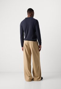 Navy sweater with a relaxed fit and a collar, paired with beige wide-leg trousers. Smooth texture and minimal detailing are visible.
