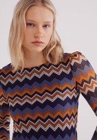 Gebreide langekleurige top met een zigzagpatroon in marineblauw, oranje en crème. De stof heeft een gestructureerde, open geweven afwerking.