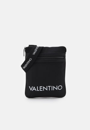 Melnais neilona maisiņš ar rāvējslēdzēju, ar logotipa siksnu un kontrastējošu baltu 'VALENTINO' tekstu priekšpusē. Gluda tekstūra.