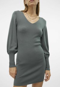 Abito lavorato a maglia grigio con scollatura a V profonda, maniche lunghe a sbuffo e polsini a coste. Design aderente con una superficie liscia.