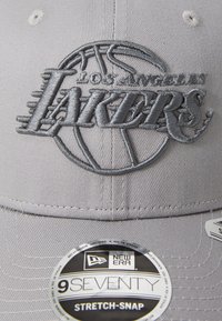 Casquette grise avec le logo brodé des "Los Angeles Lakers", design de basketball, tissu texturé, visière incurvée et étiquette circulaire New Era sur le côté.