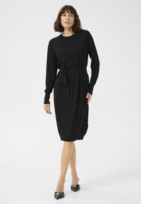 Schwarzes Strickkleid mit rundem Halsausschnitt, langen Ärmeln, einem Taillengürtel und einem mittellangen Saum. Die Textur ist glatt und enganliegend.