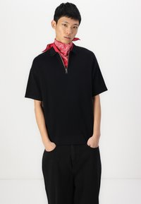 Black short-sleeve polo shirt with a zippered collar, paired with black pants. Accessories include a red paisley bandana tied around the neck.