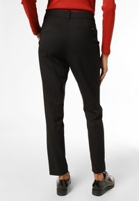 Un pantalon noir sur mesure avec une texture lisse, coupe ajustée et poches arrière. La tenue est accompagnée d'un haut rouge contrastant et de chaussures noires.