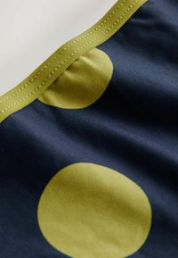 Navy stof met grote olijfgroene stippen en een zachte textuur, met een contrasterende groene gestikte rand aan de bovenkant.
